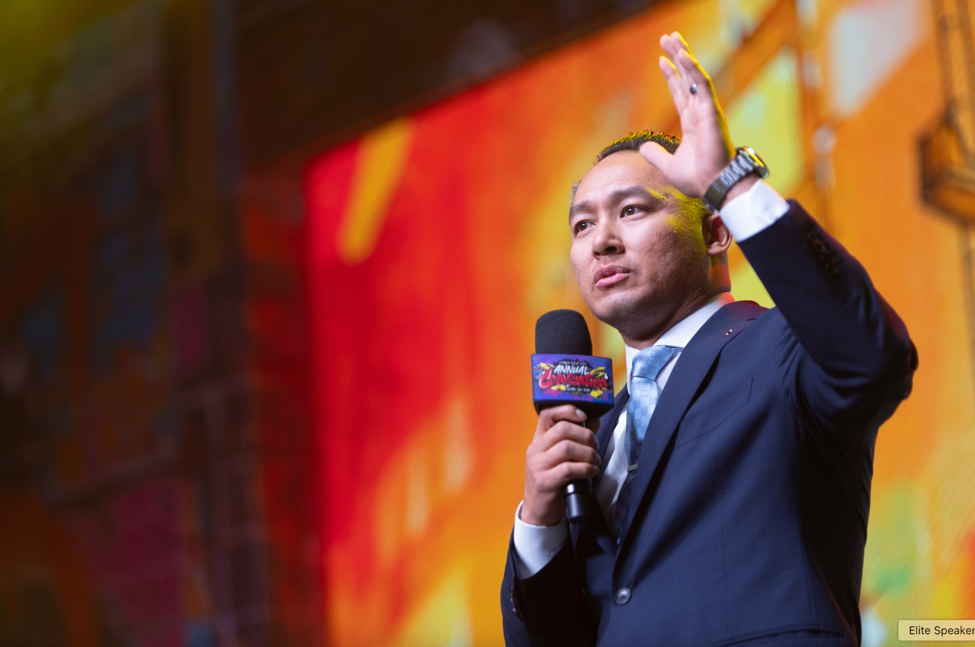 Keynote speaker on a dark stage in front of a packed audience